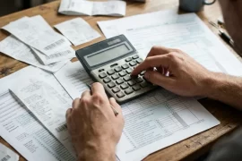Manos usando una calculadora sobre formularios de impuestos y recibos en un escritorio