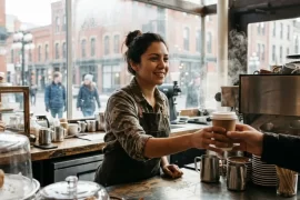 Barista latina atendiendo a un cliente en una cafetería de Canadá, empleo con salario mínimo